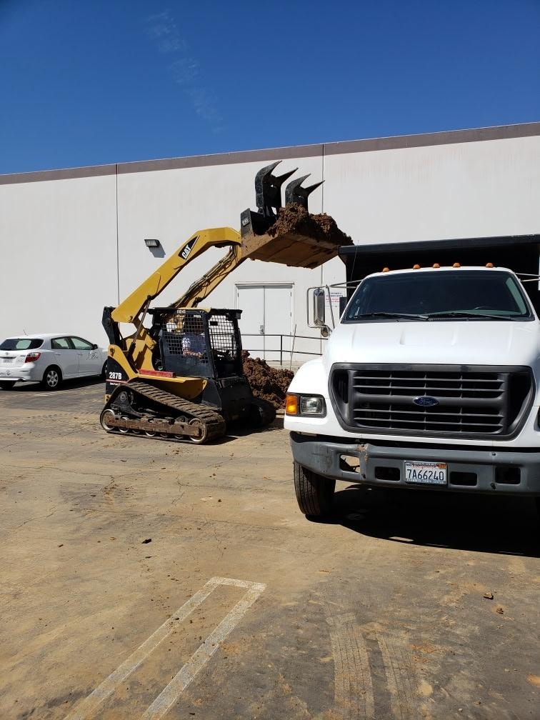 CAT skid steer loading excavated soil into dump truck — commercial waterline repair Orange County CA