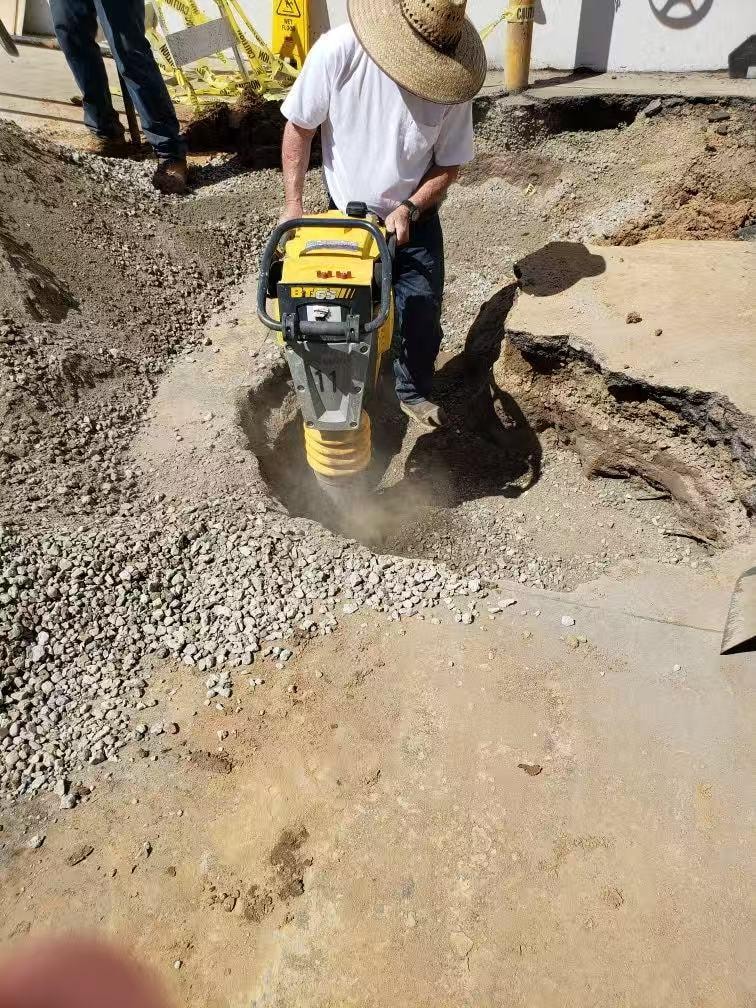 Worker operating plate compactor during waterline repair — Orange County CA