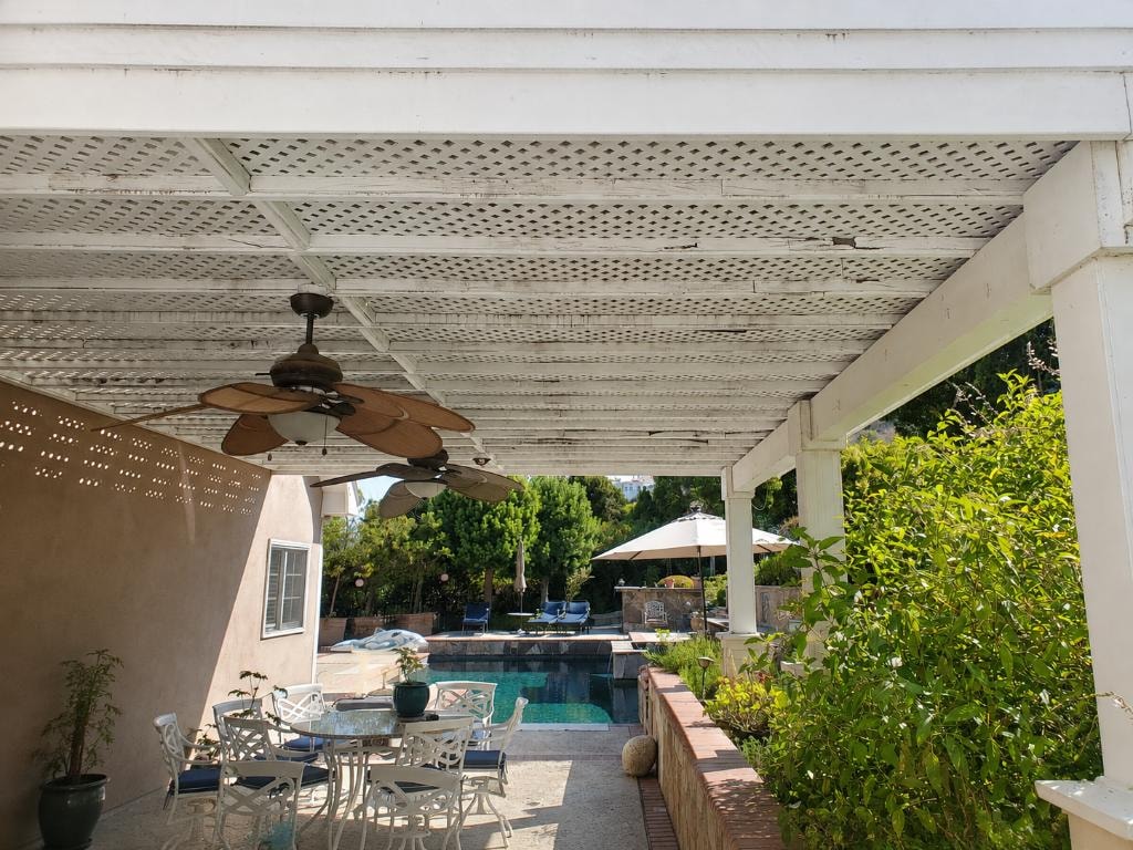 Original white lattice patio cover interior with ceiling fans and pool view — Orange County CA